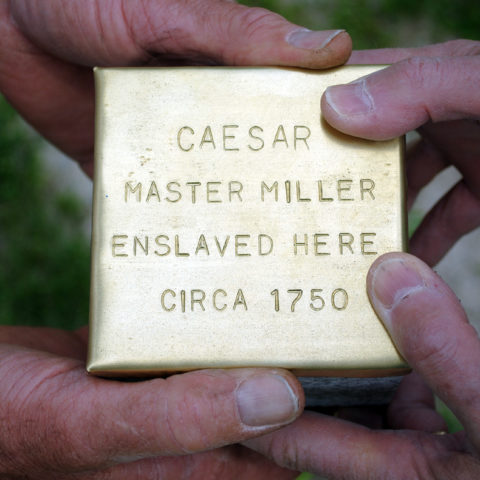 Two sets of hands holding a brass Touching Stones plaque