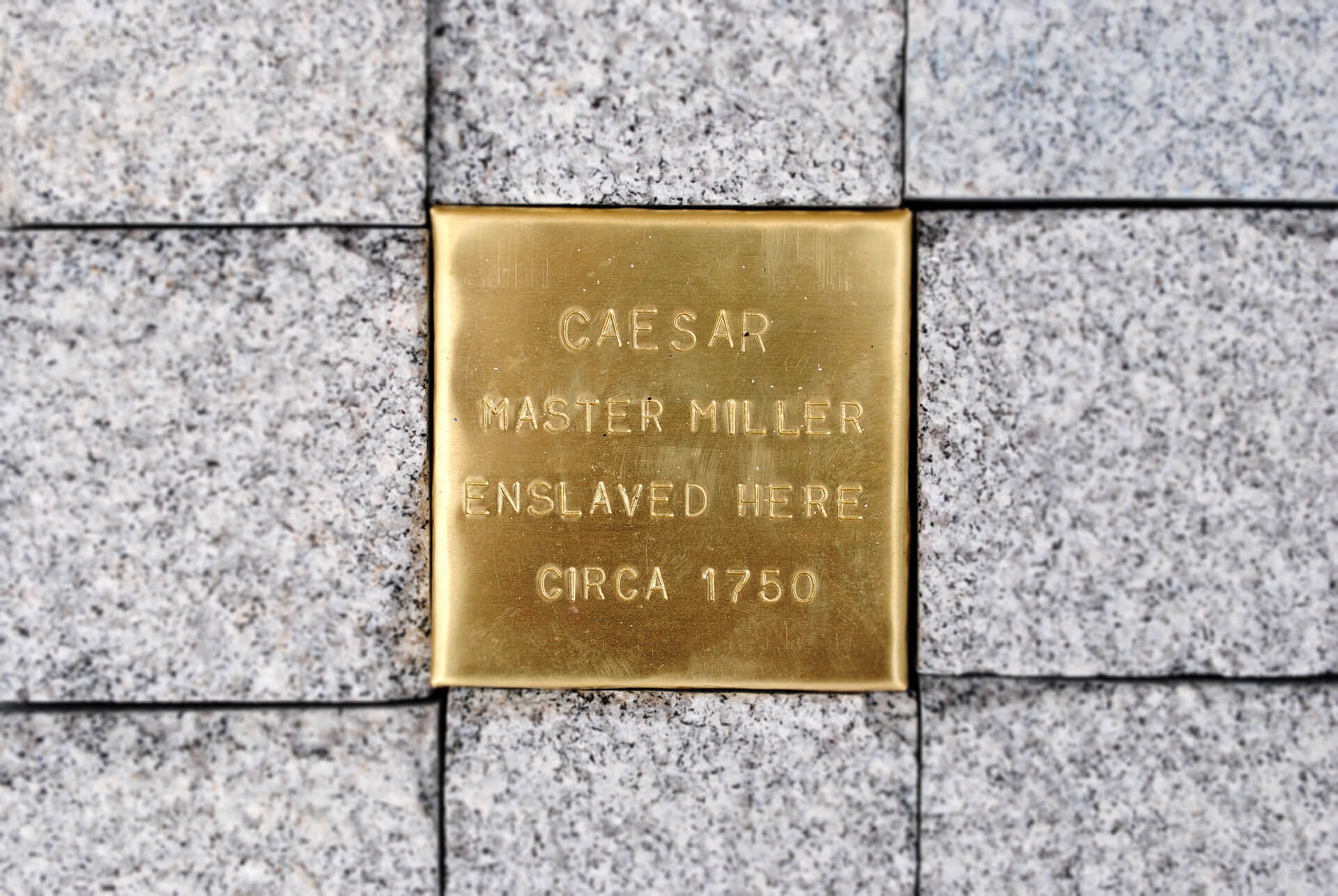 Commemorative plaque inlaid in cobblestone street and showing the name of a slave