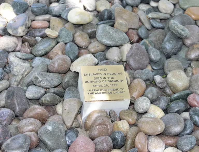 Memorial plaque for Ned, honoring his legacy in the Burning of Danbury, set among stones.