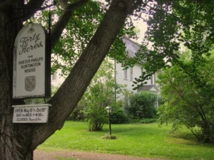 Sign for Forty Acres Porter-Phelps-Huntington House amidst lush green trees, with a historic house in the background.