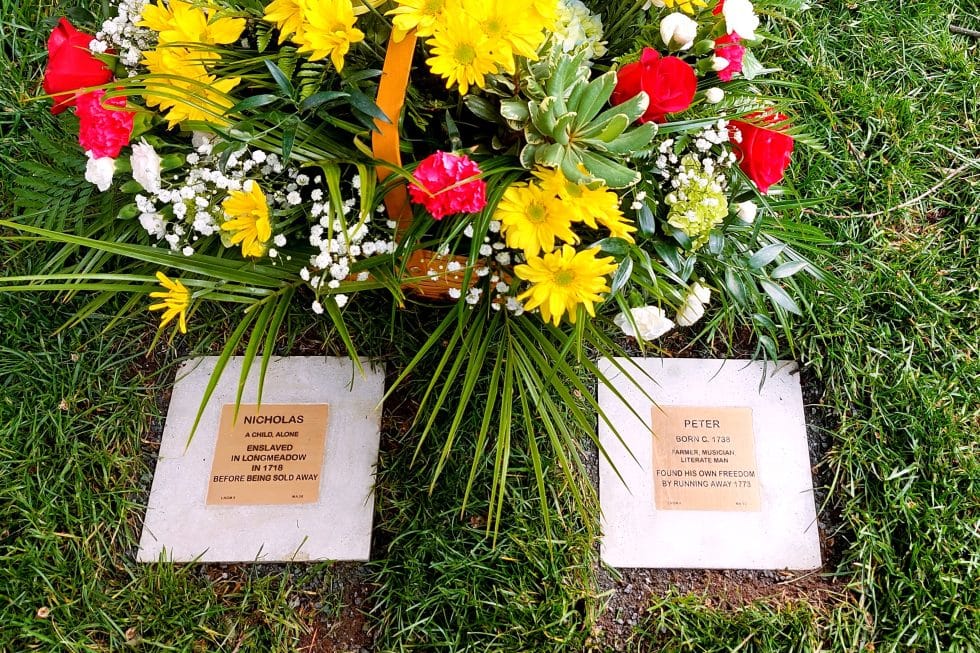 Memorial plaques for Nicholas and Peter, surrounded by vibrant flowers on a grassy lawn.