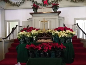 Church altar decorated for Christmas with red and white poinsettias, a cross, and a nativity scene.