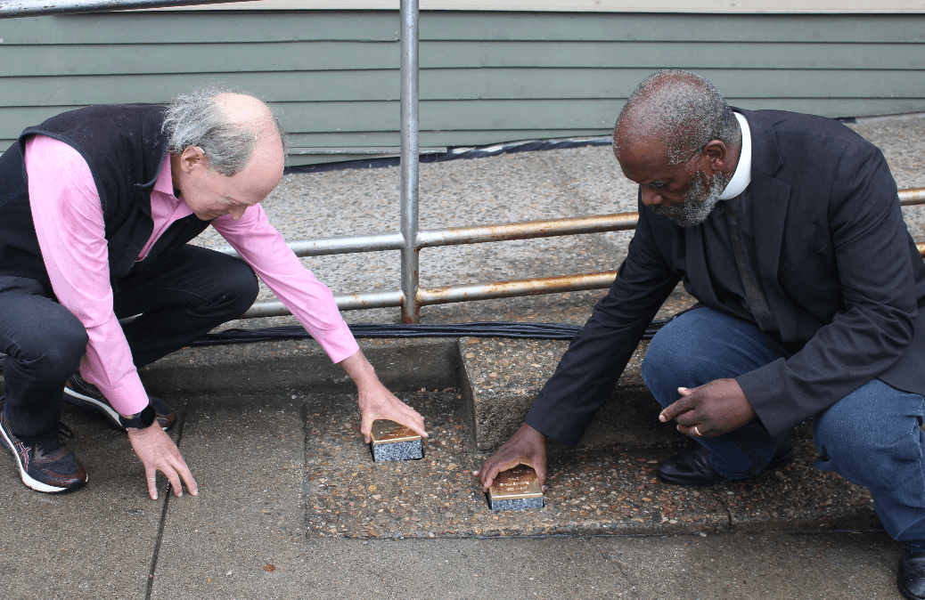Two people kneel and place engraved plaques in a paved sidewalk, engaging in a commemorative event.